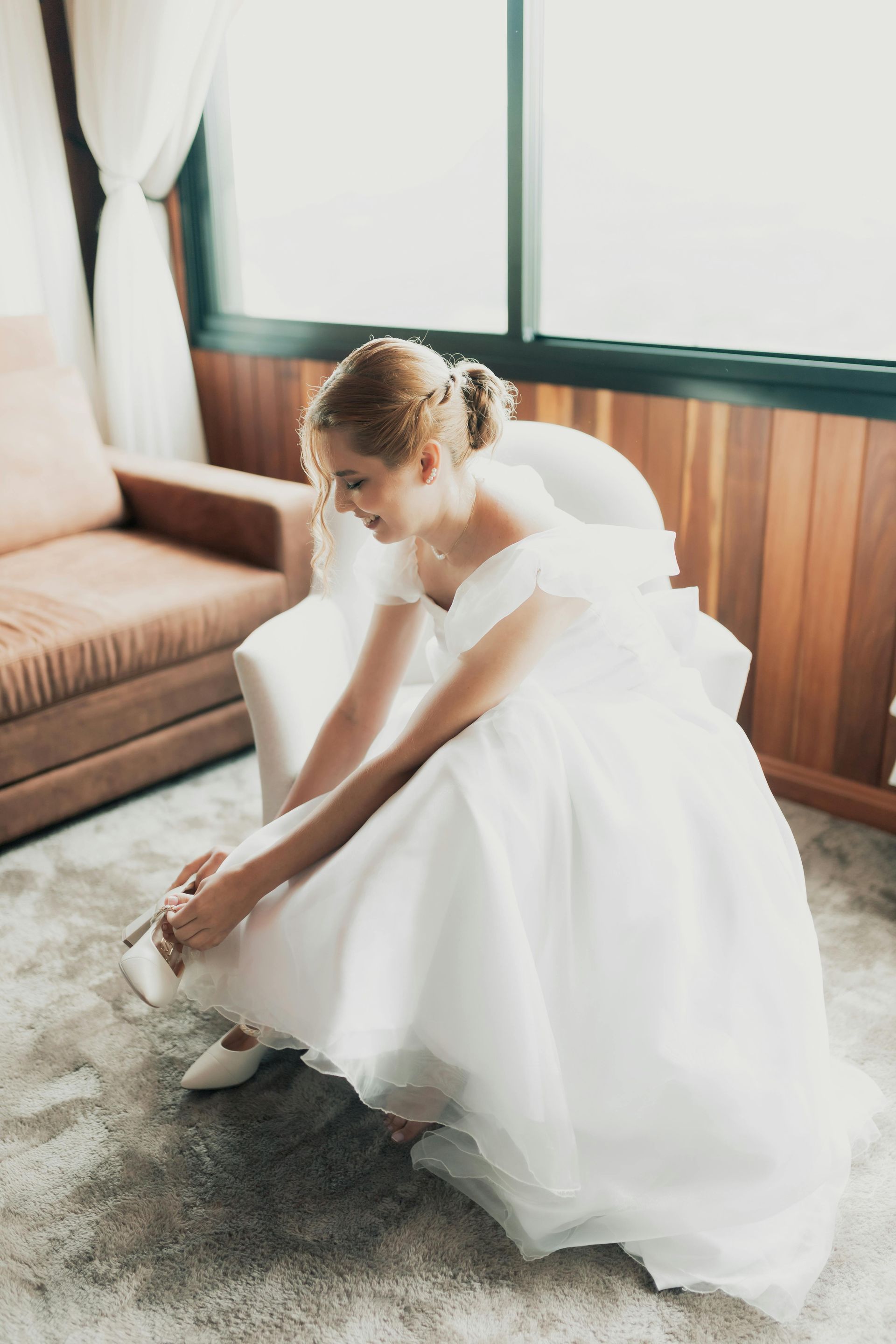 A woman in a wedding dress is sitting on the floor tying her shoes.