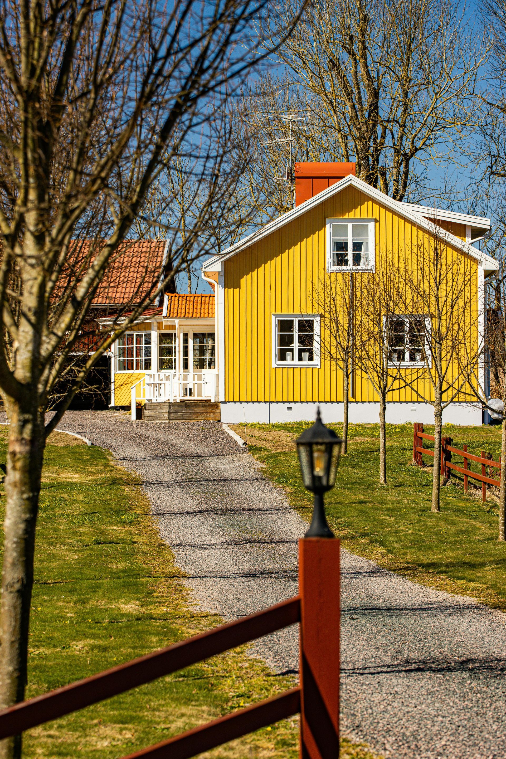 A yellow house with a red fence and a gravel driveway leading to it.