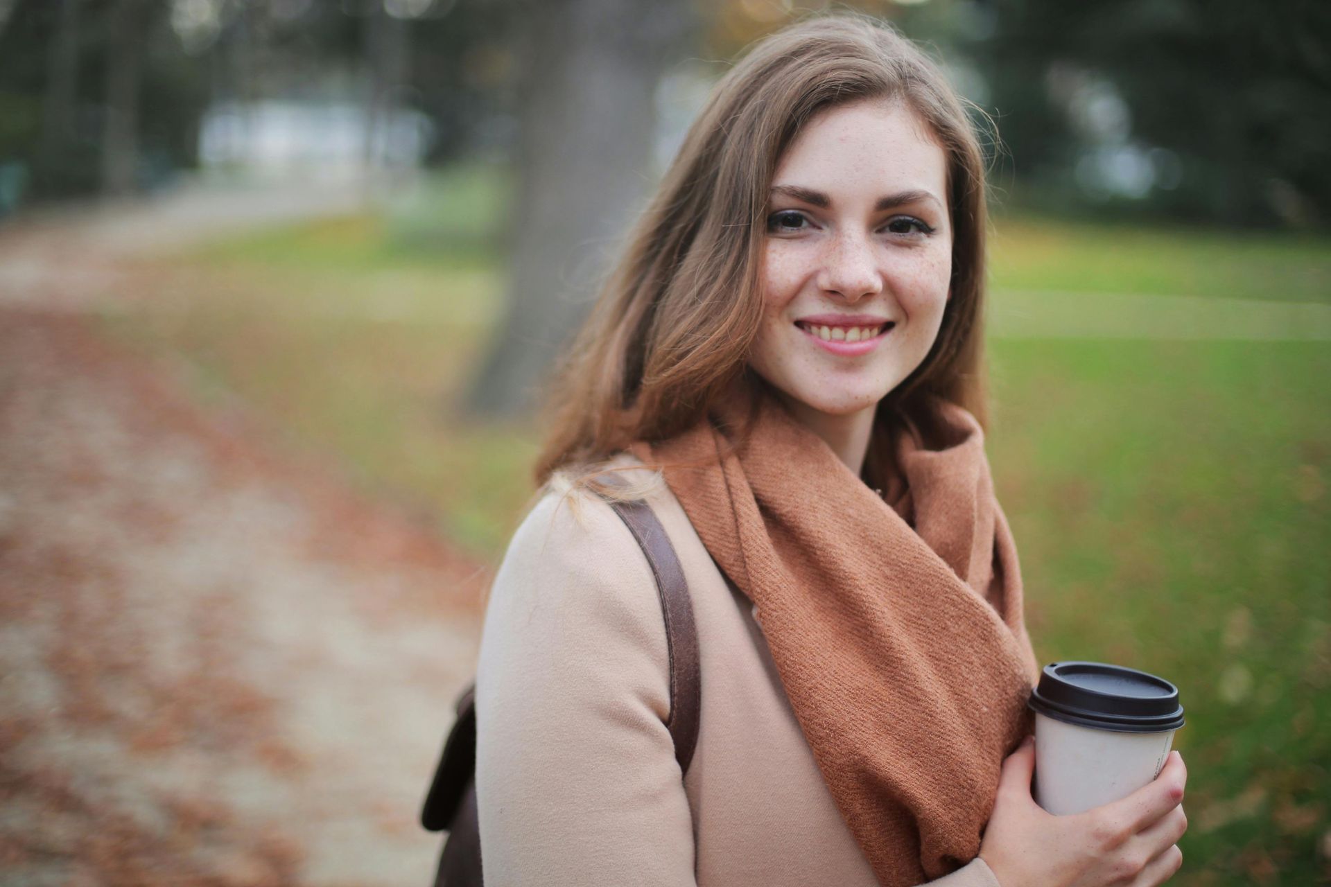 A woman is holding a cup of coffee in a park.