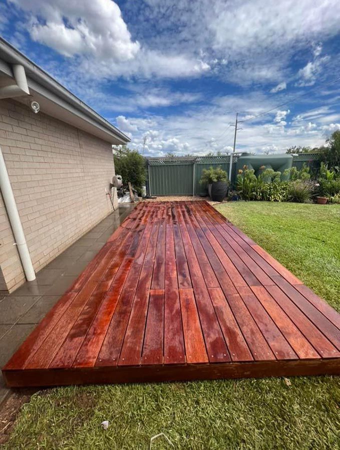 A Large Wooden Deck is Sitting on Top of a Lush Green Lawn in Front of a House — B & C Yard Improvements in Dubbo, NSW