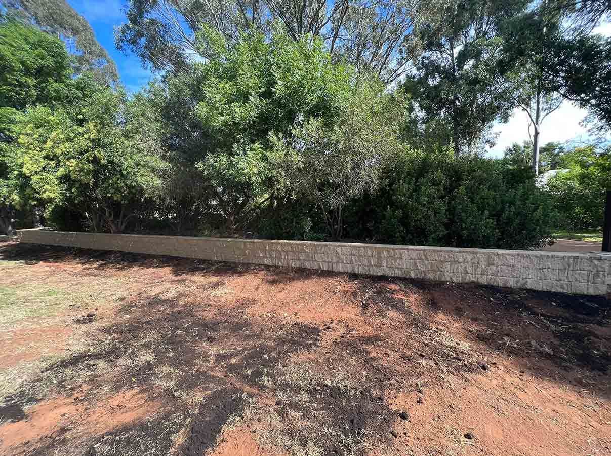 A Stone Wall Surrounds a Dirt Field With Trees in the Background — B & C Yard Improvements in Dubbo, NSW