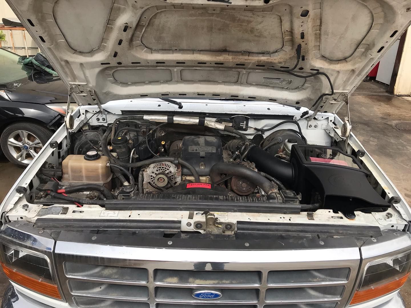 A car is being repaired in a garage with tires in the background.