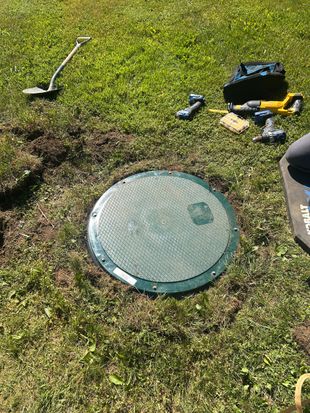 Worker lowering a concrete well ring with a chain hoist in a muddy outdoor area
