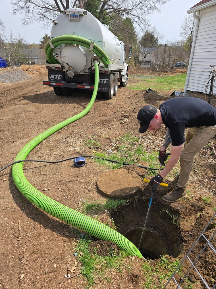 Worker clearing a thick green hose from a muddy trench beside a white truck in a rural field