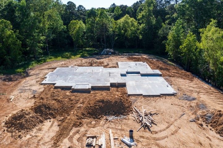 Aerial view of a concrete foundation being built on a cleared site beside dense trees.