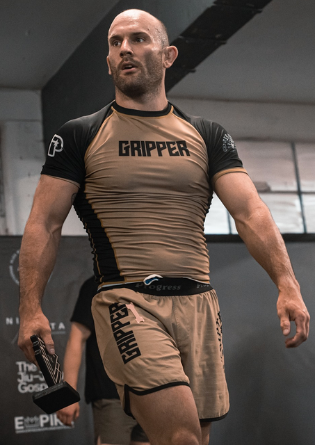 a man with a beard is wearing a gripper shirt and shorts .