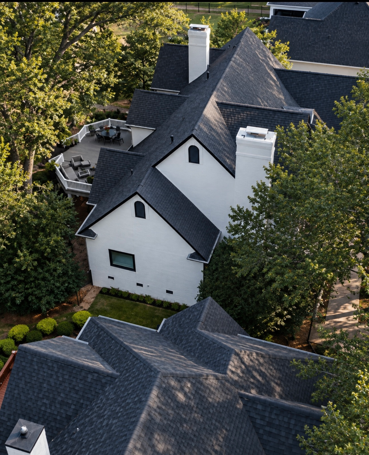 Aerial view of white houses with dark gray roofs surrounded by trees.