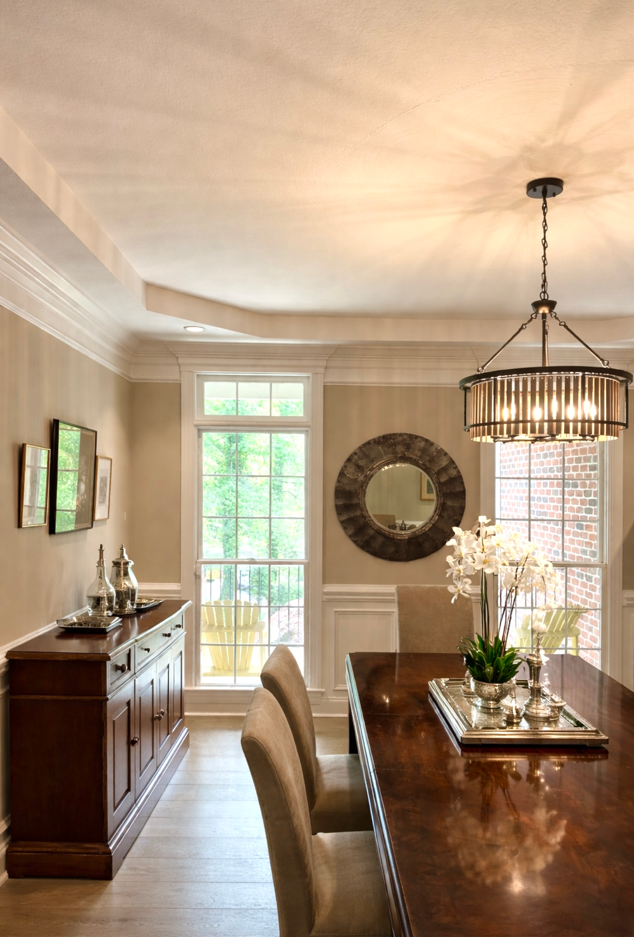 Elegant dining room with a long wooden table, upholstered chairs, sideboard, and large round wall mirror.