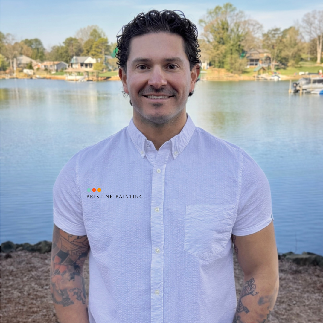 Smiling person in a white shirt standing by a lake with trees in the background