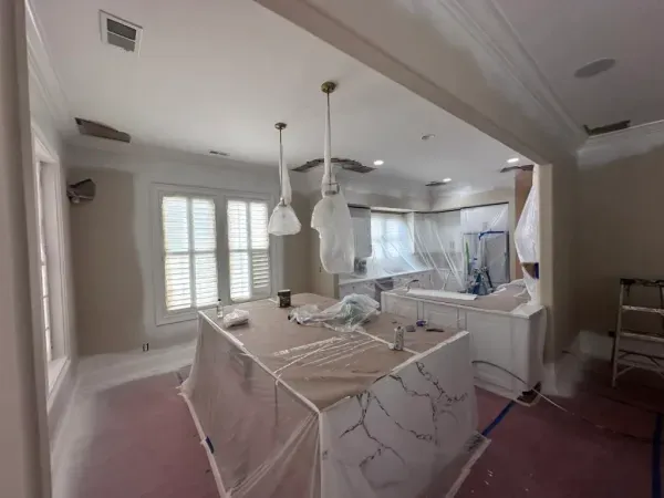 Living room under renovation with covered furniture, white walls, and hanging light fixtures