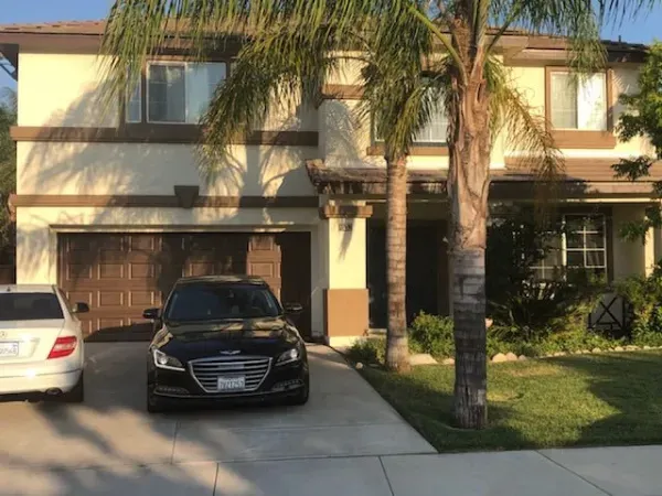Two-story suburban house with palm trees, a driveway, and two parked cars in front.