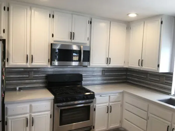 White kitchen with stainless steel appliances, black stove, and gray backsplash tiles