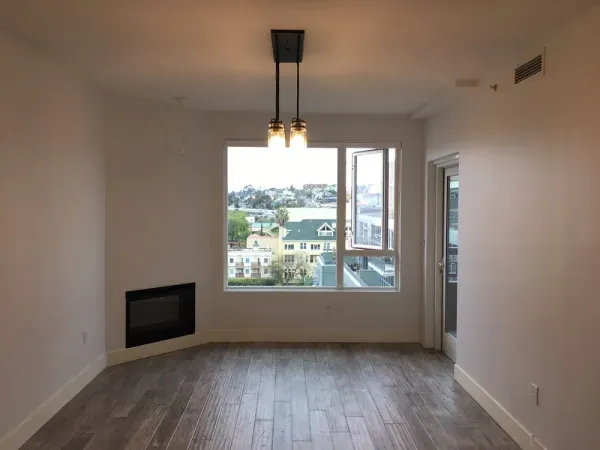 Empty living room with wood floors, fireplace, and large window overlooking a neighborhood view