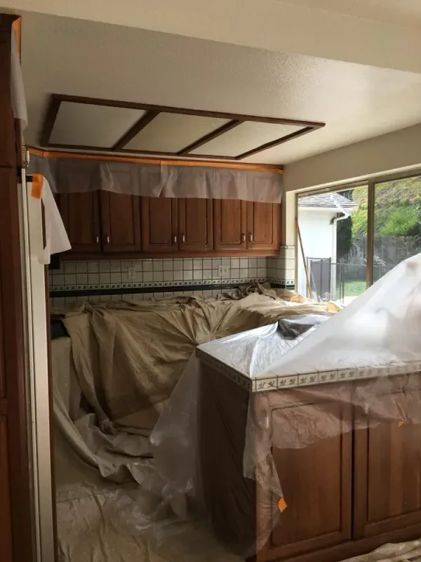 Kitchen under renovation with cabinets and counters covered in protective plastic and drop cloths.