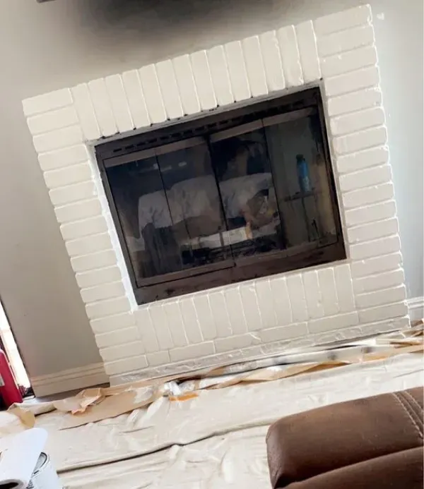 White tiled fireplace with a dark glass insert in a living room; floor covered with a protective drop cloth.