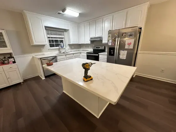 Bright white kitchen with island, stainless steel fridge, and a yellow drill on the countertop.