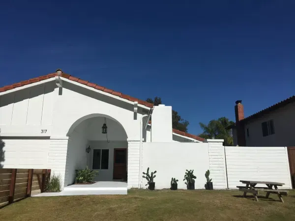 White house with red-tile roof, arched entry, and small front yard under a clear blue sky