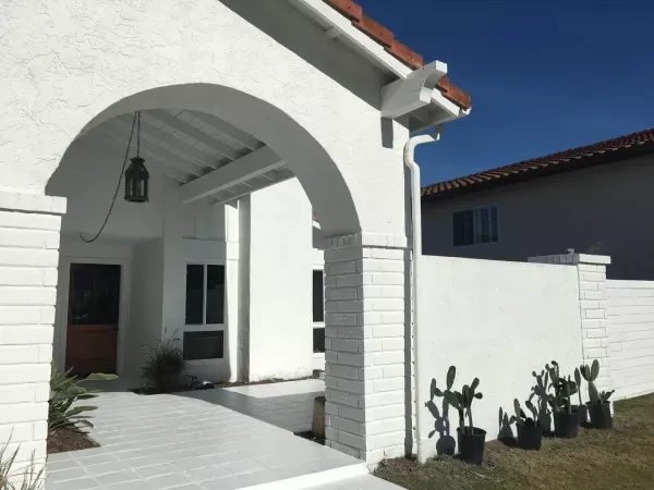 White stucco house entry with arched porch, hanging lantern, and potted cacti by a bright blue wall