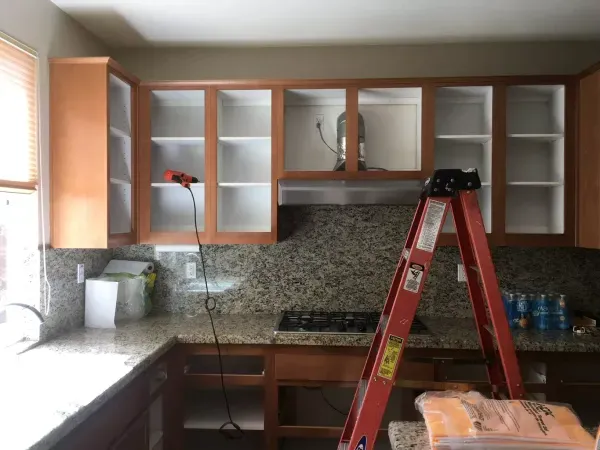 Kitchen cabinets being installed, with a red ladder in front of unfinished upper cabinets.
