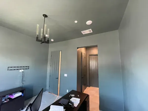 Home office with gray walls, dark ceiling, black chair, and open doorway to a lit hallway