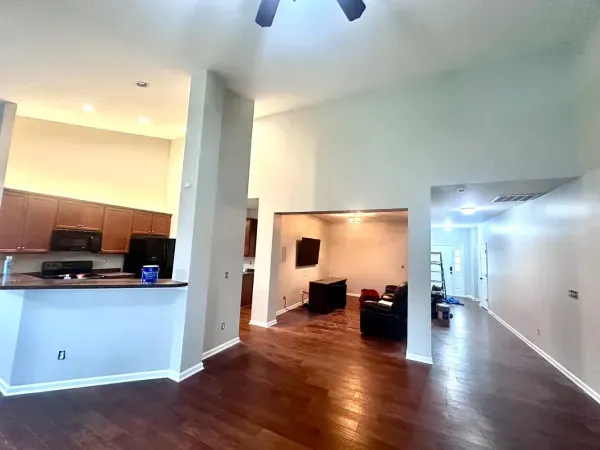 Open-plan living room with hardwood floors, kitchen counter, and a hallway leading to another room.
