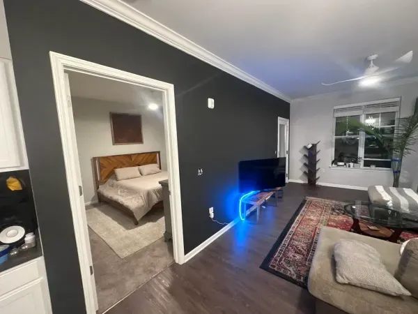 Modern living room with dark accent wall, TV glow, patterned rug, and a bedroom visible through an open doorway
