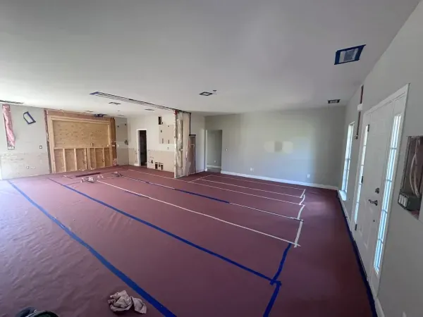 Empty living room under renovation, with red floor covering and blue tape lines.