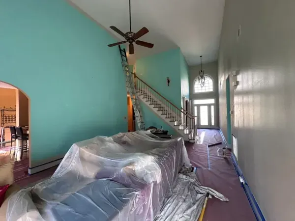 Living room with turquoise walls, a staircase, and furniture covered in plastic during renovation