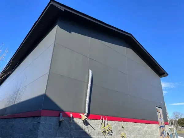 Gray building with a red stripe and black roof against a blue sky