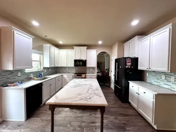Bright white kitchen with marble island, gray cabinets, tile backsplash, and dark wood floor