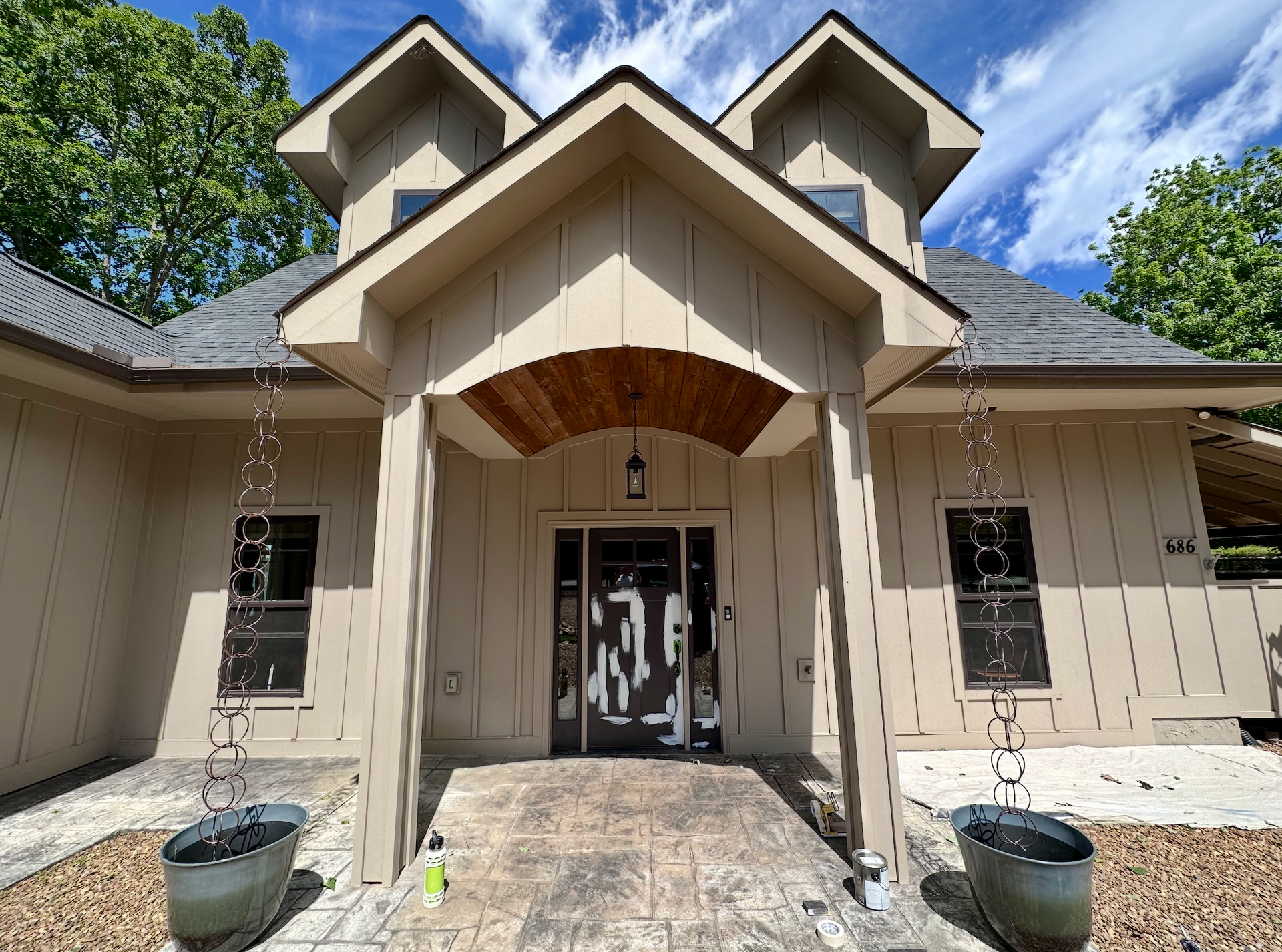 Front entrance of a beige house with a stone walkway, arched porch, and double glass doors under a blue sky