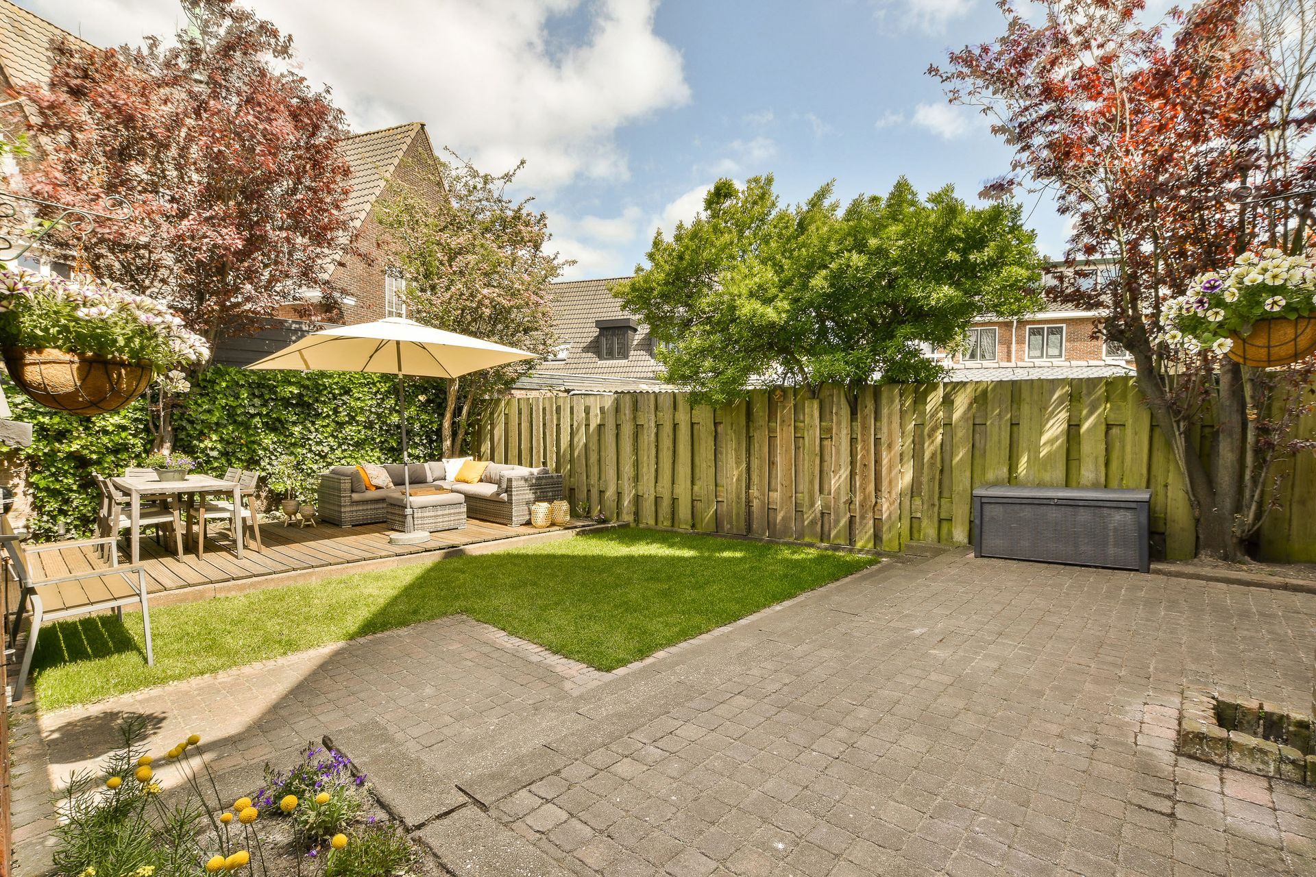 Backyard patio with gravel area, wooden fence, patio umbrella, and flower beds on a sunny day