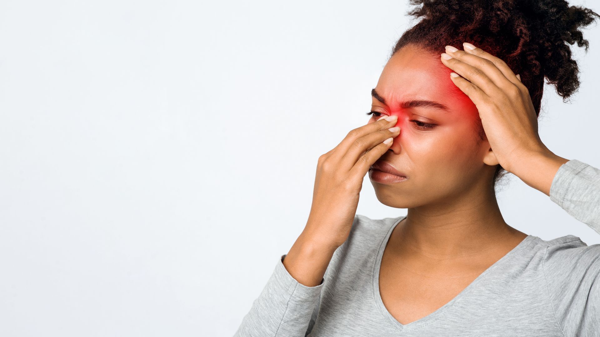 Person holding their forehead and nose with a red, painful-looking forehead against a white background