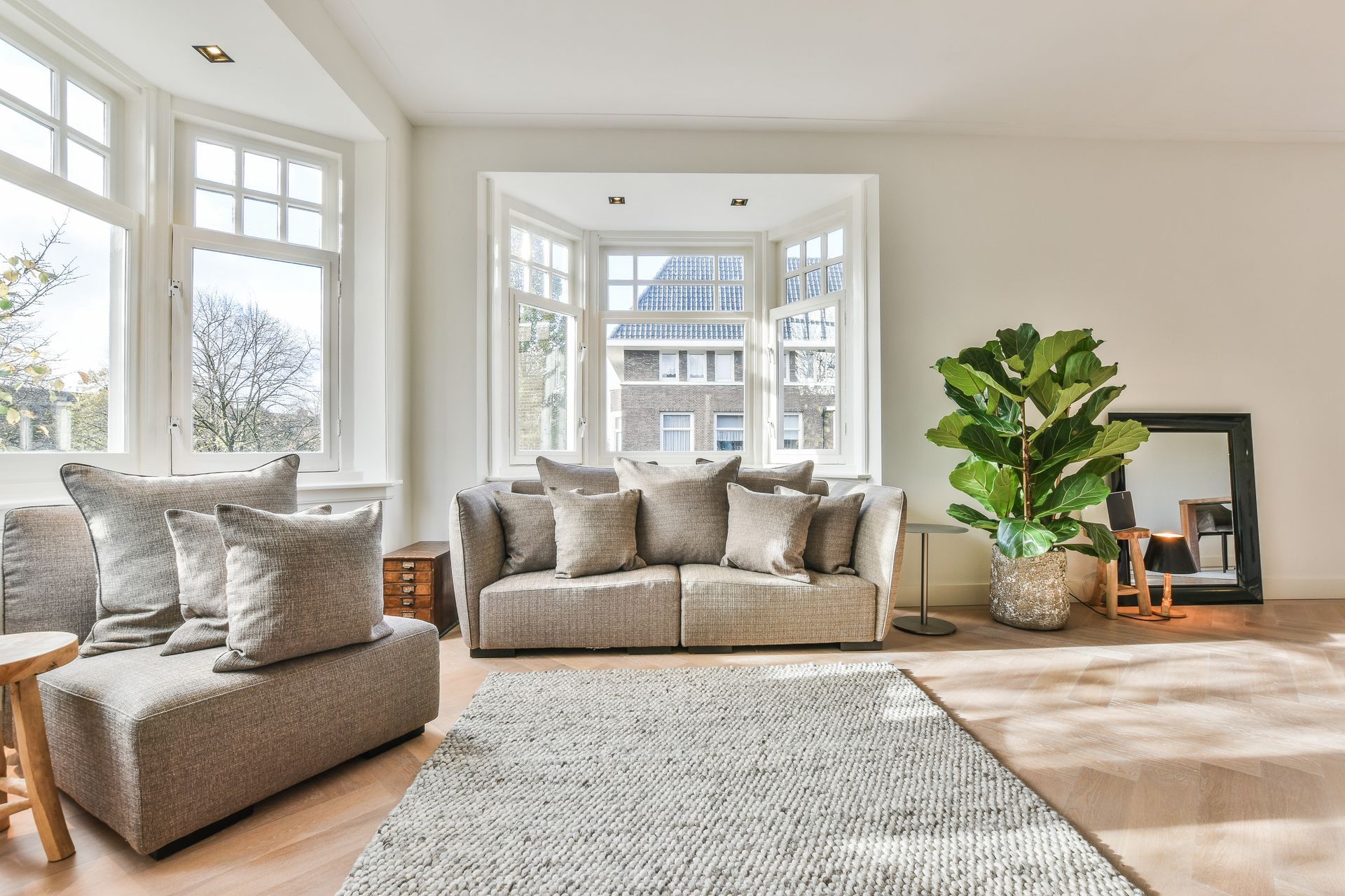 Bright living room with gray sofas, large windows, a potted plant, and a light rug in sunlight