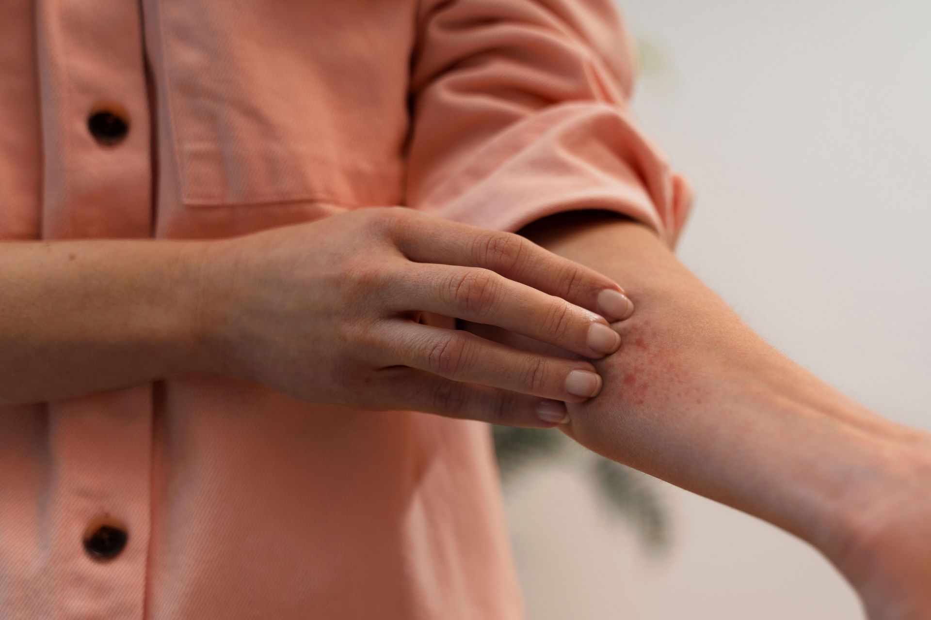Hands rubbing a forearm on a peach shirt against a blurred background