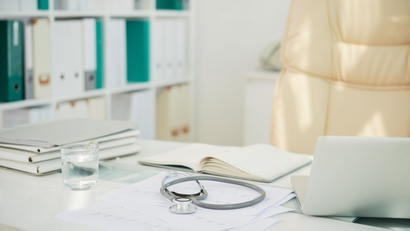 Bright office desk with stethoscope, notebook, laptop, and shelves in the background