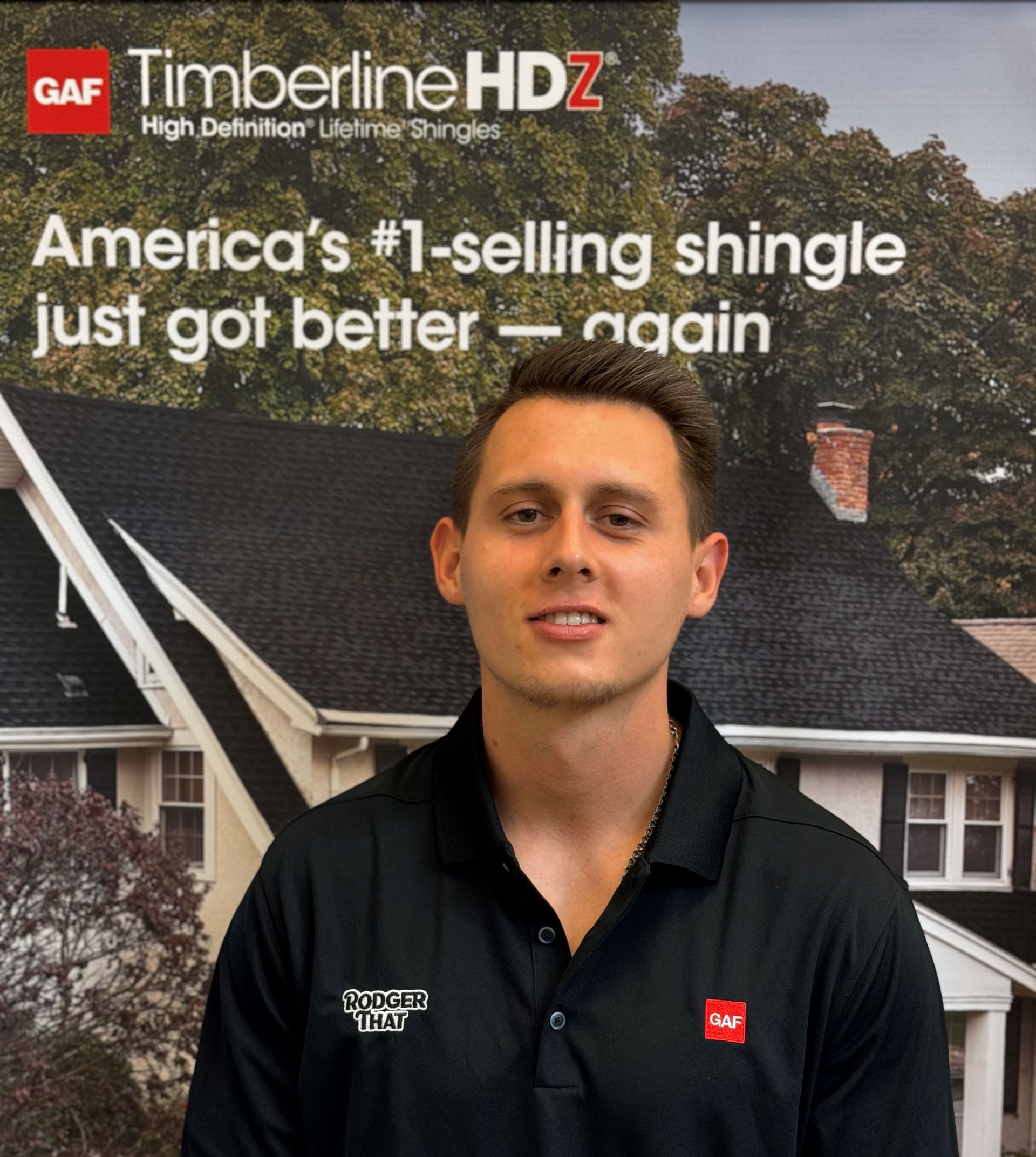 Man in black polo standing before GAF Timberline HDZ roofing display with “America’s #1-selling shingle” text