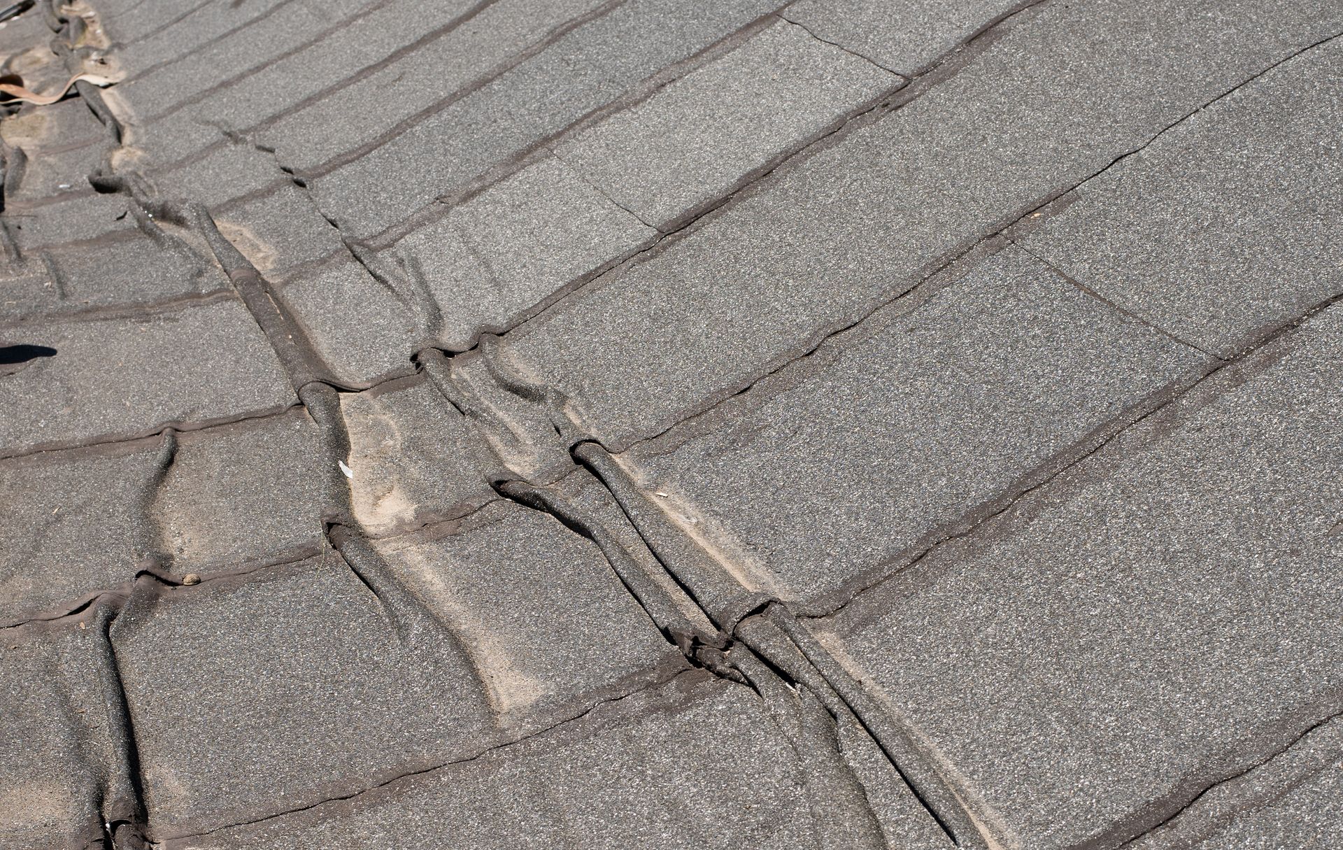 Close-up of cracked gray roof shingles with damaged seams and worn patches