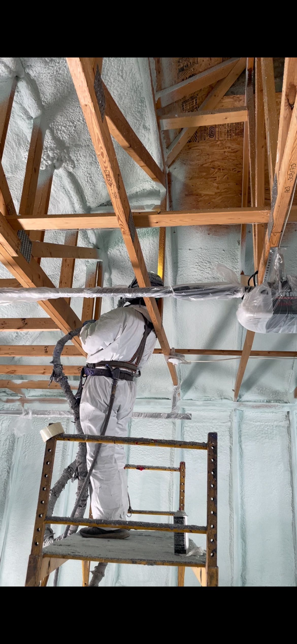 A man is spraying insulation on the ceiling of a building.