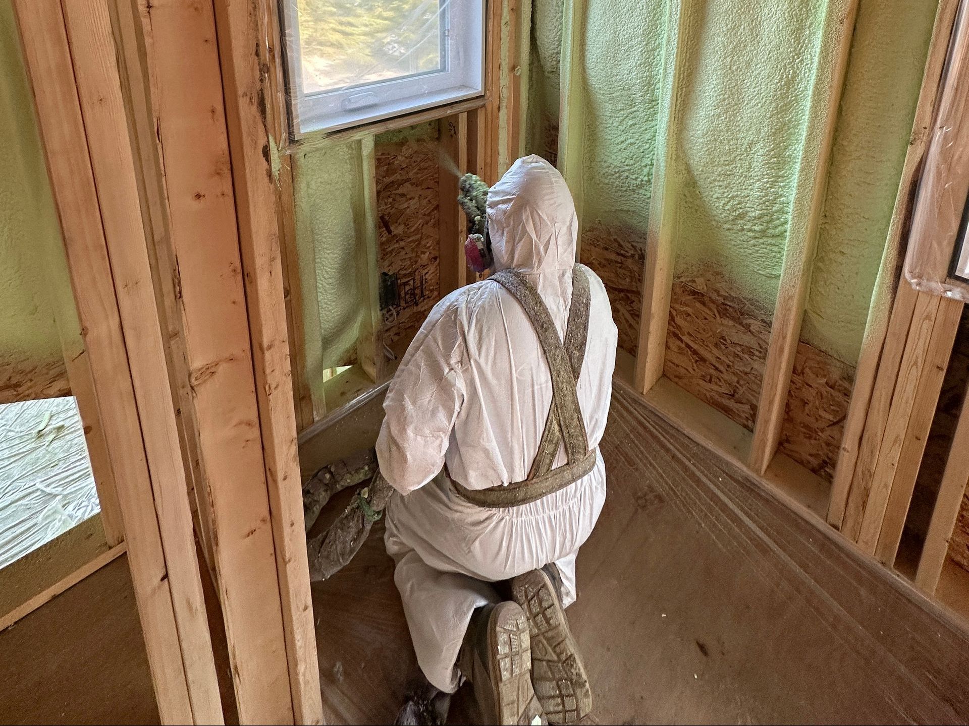 A man in a protective suit is spraying insulation on a wall.