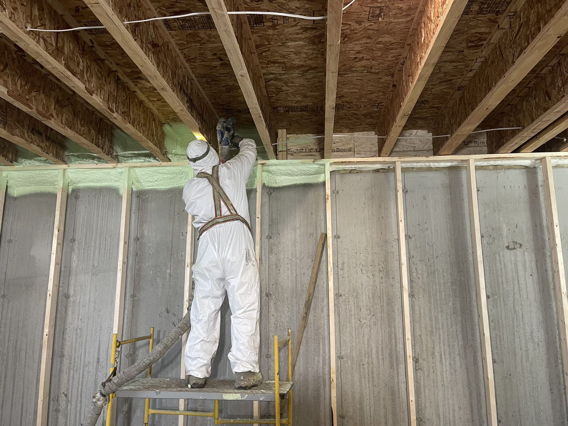 A man in a protective suit is spraying insulation on a wall.