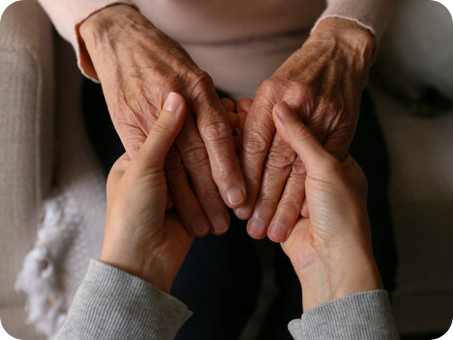 Two hands gently holding an older person’s wrinkled hands in a comforting gesture