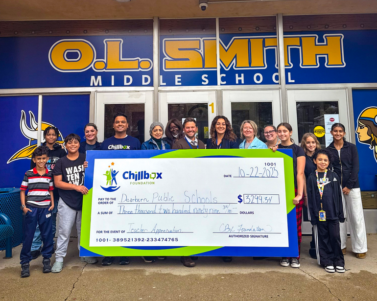 Group of people holding a large check outside O.L. Smith Middle School entrance