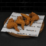 Fried chicken wings on BirdBox-branded paper atop a round wooden board against a dark background