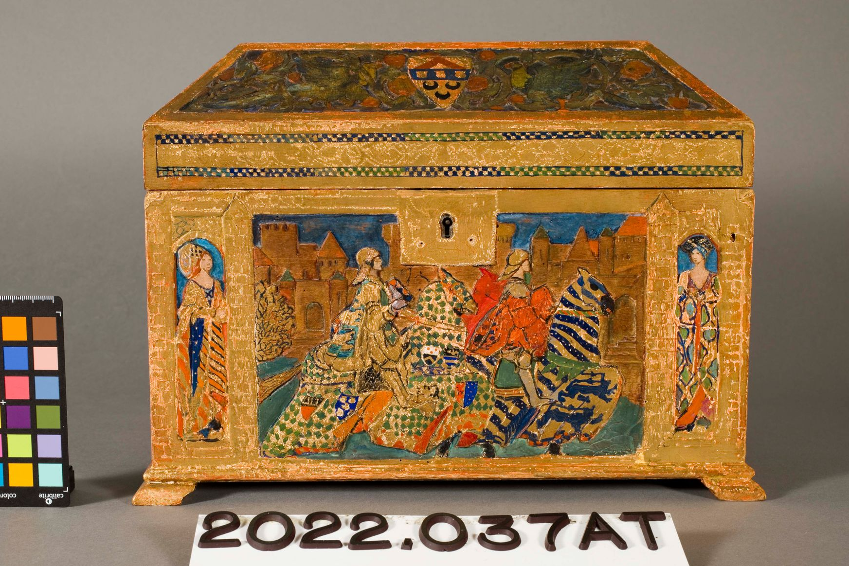 An ornate, gold-painted wooden box featuring a central painted scene of figures on horseback and two standing figures.