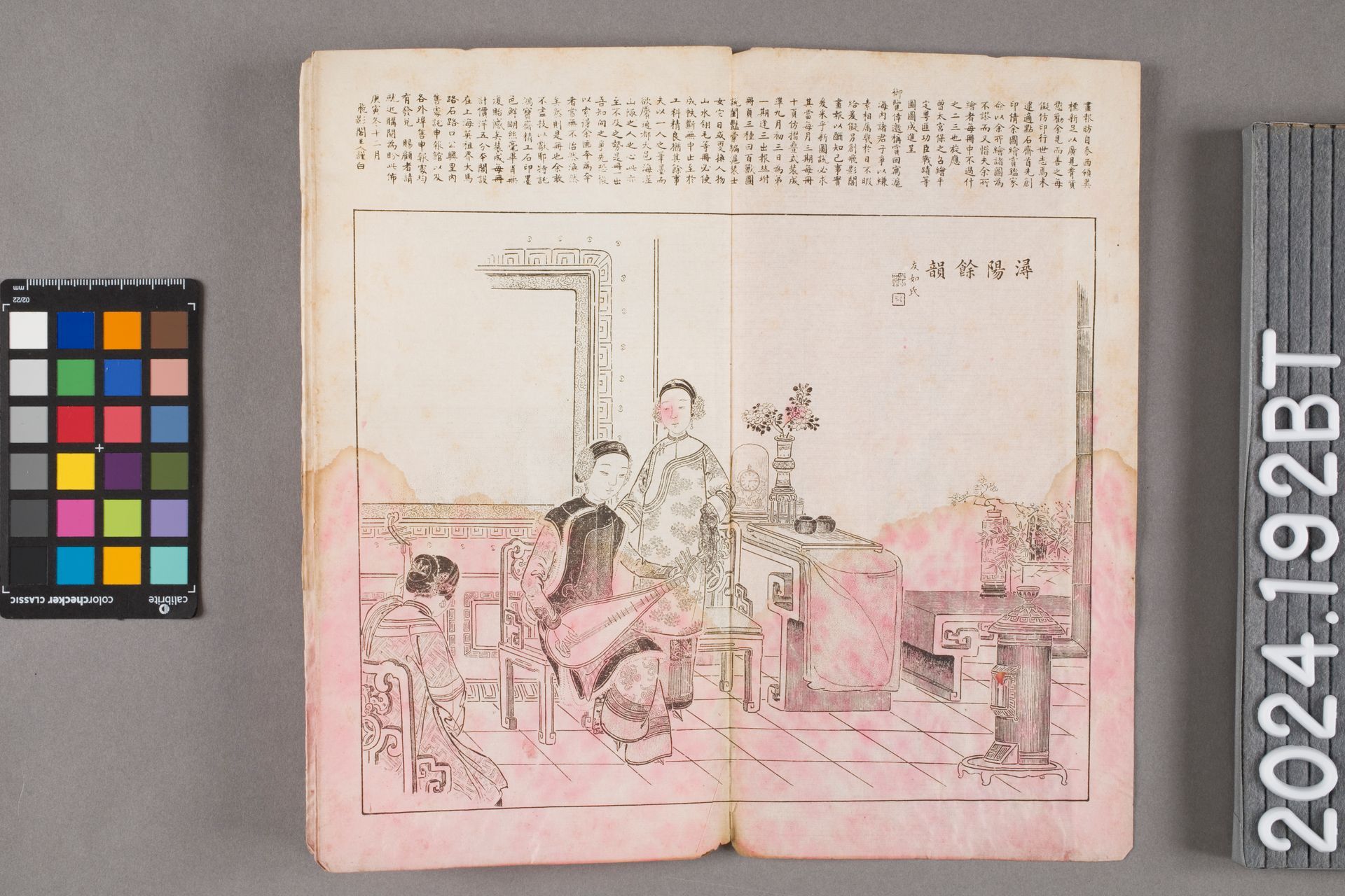 An open book with Japanese text, a color chart, and a woodblock print of figures in a patterned room.