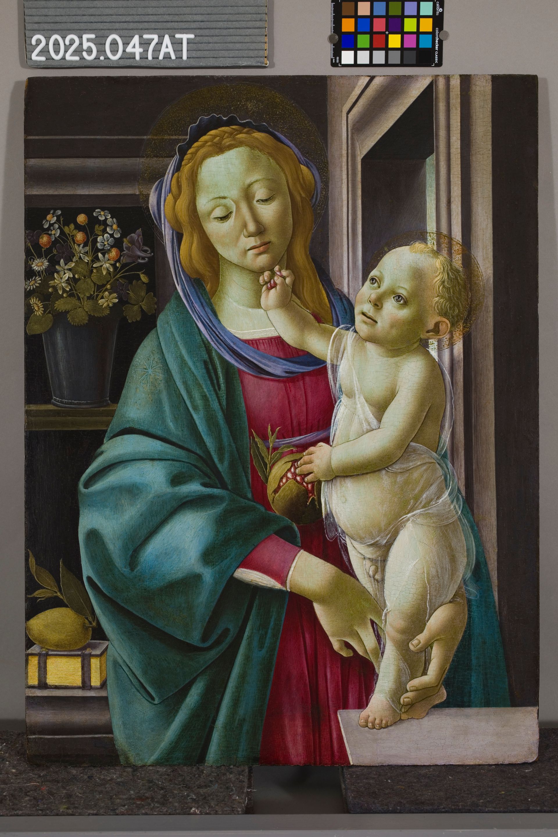 Renaissance painting of a woman in a blue cloak holding a child, with flowers and fruit on a shelf in the background.