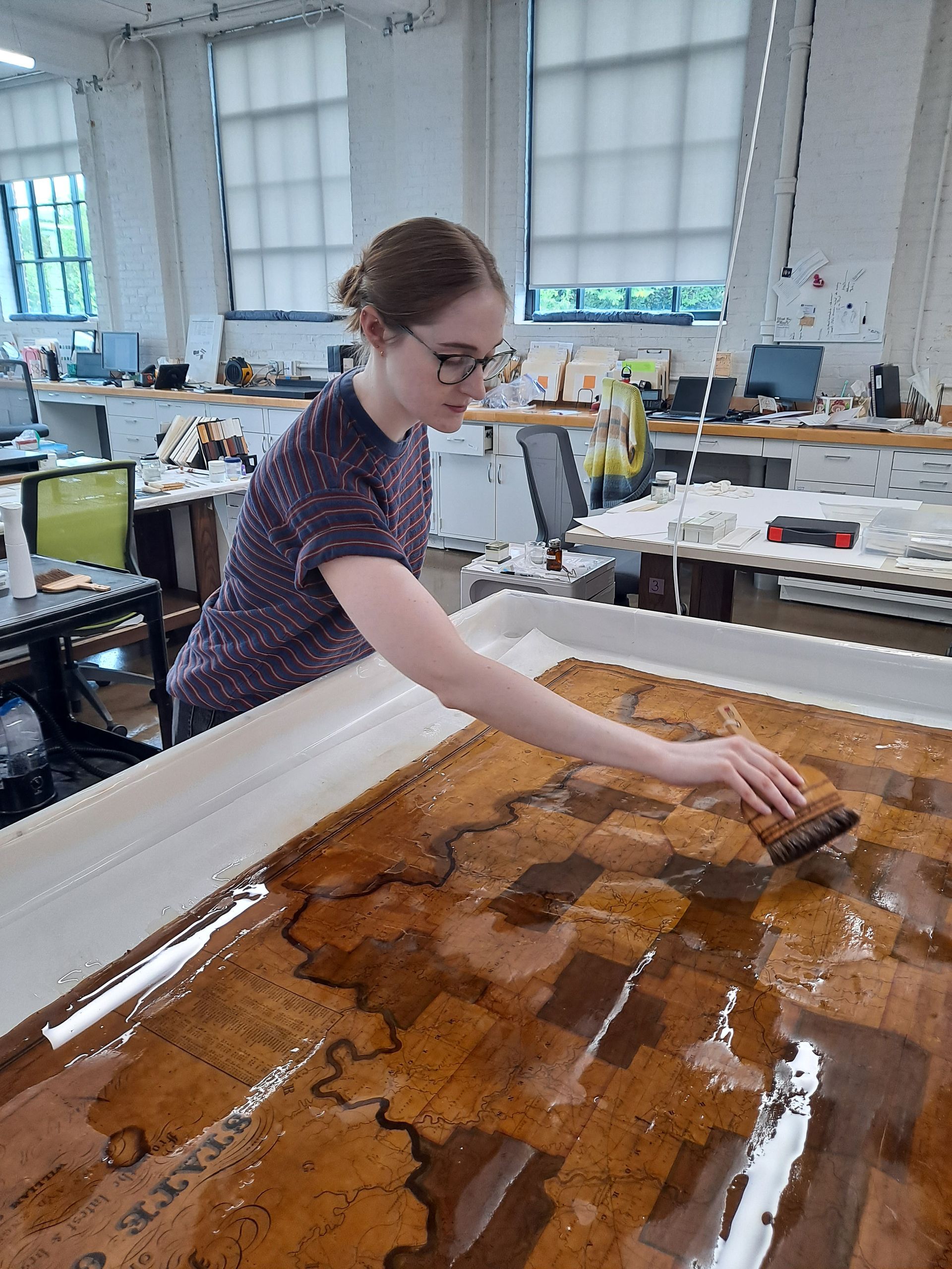 Person cleaning a large amber resin surface in a bright workshop with tools and worktables.