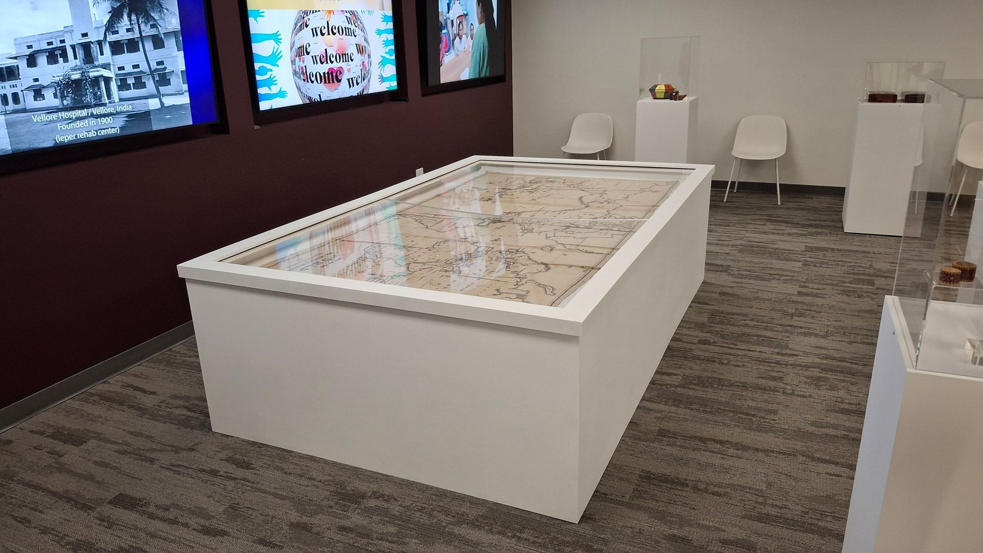 A museum exhibit featuring a central white display table with an intricate tiled floor, flanked by screens and pedestals.