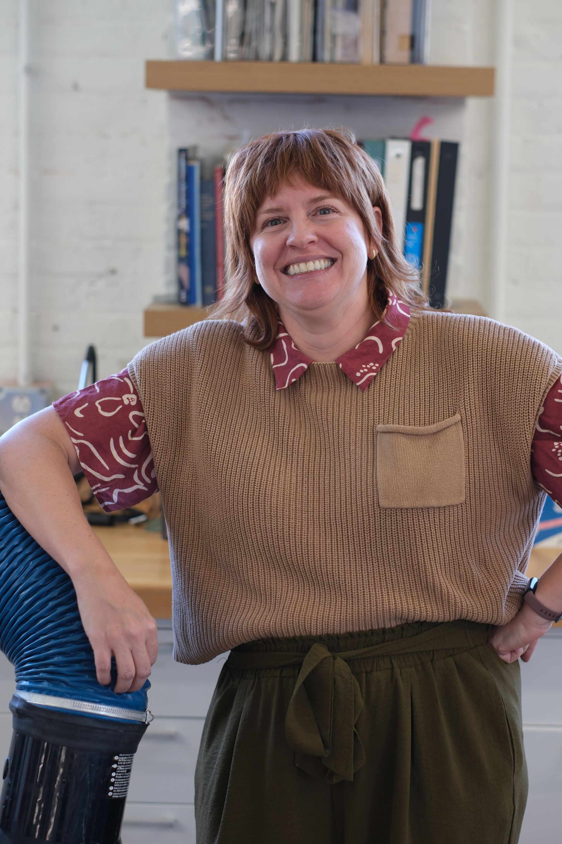 A woman wearing a denim shirt and a brooch is smiling for the camera.